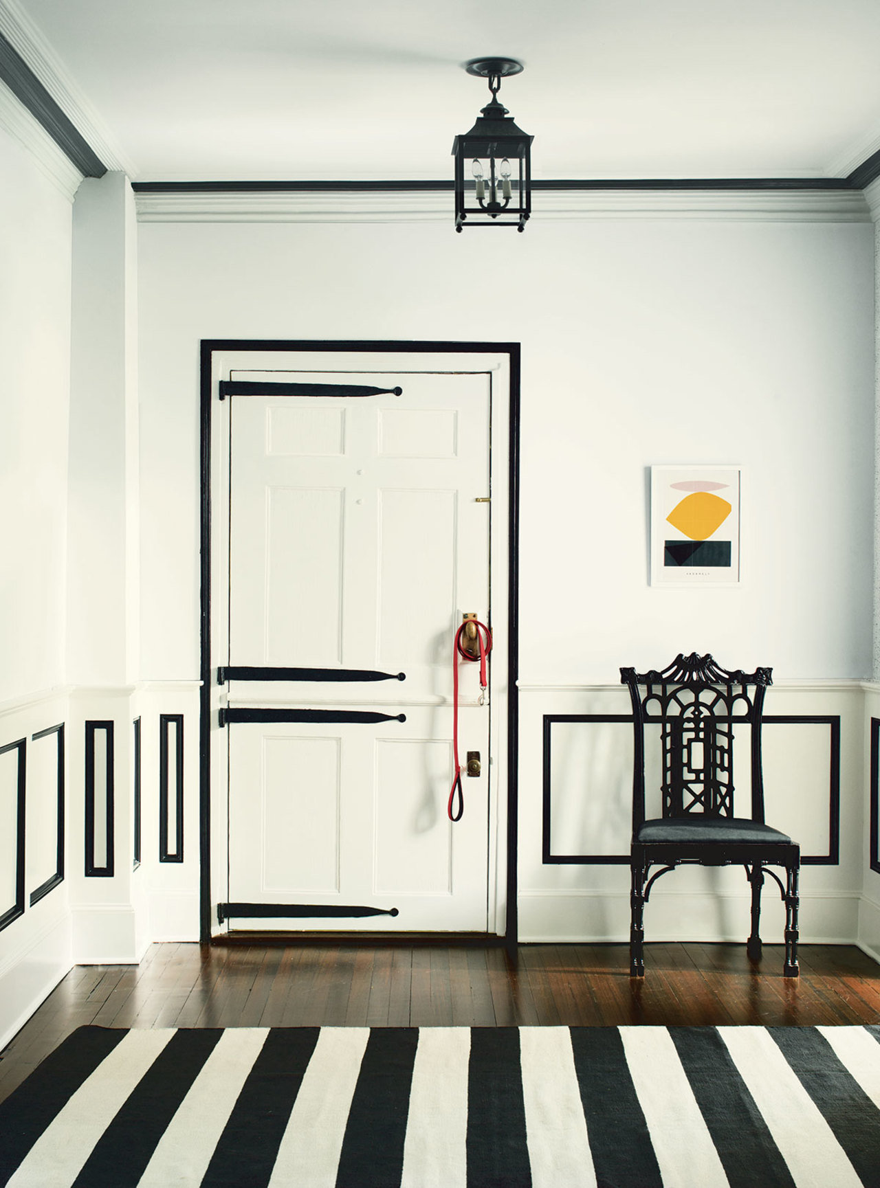 This white foyer has a graphic pop by way of black trim and detailing on the walls and door.
